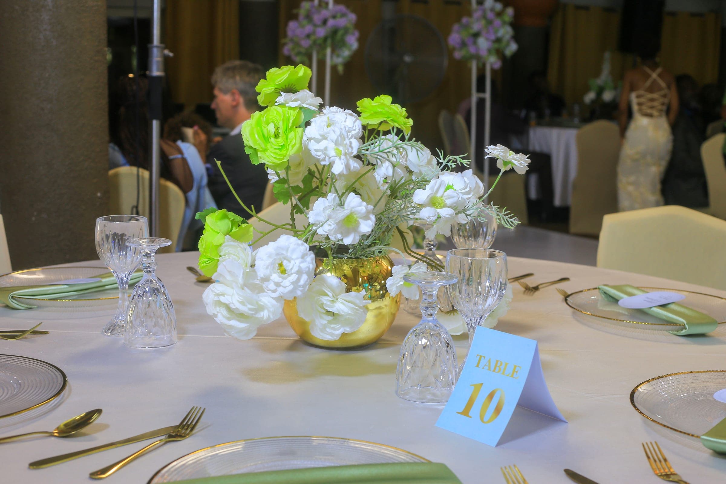 Round table set with green napkins, gold cutlery and white florals
