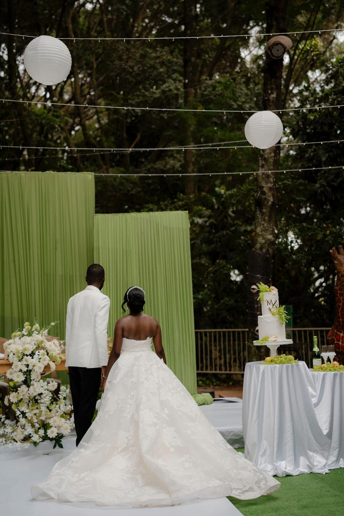The couple at the cake table in front of a green drape